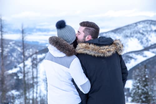 Groom kisses his bride on the cheek as she looks out at the mountains during their mountain top wedding