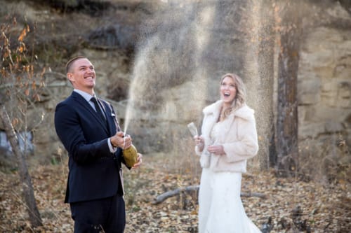 Groom pops champagne during a Calgary wedding as the bride looks joyfully on