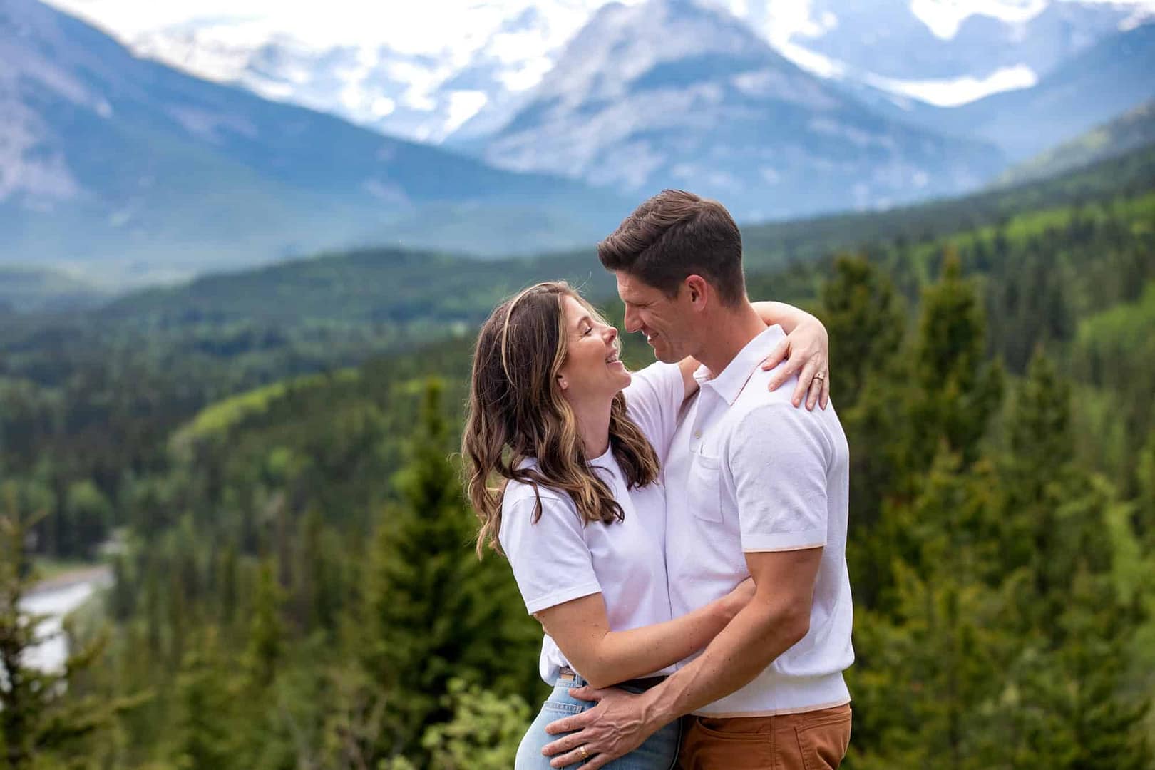 Couple hugs during a candid photography moment with their engagement session with Kananaskis mountains behind